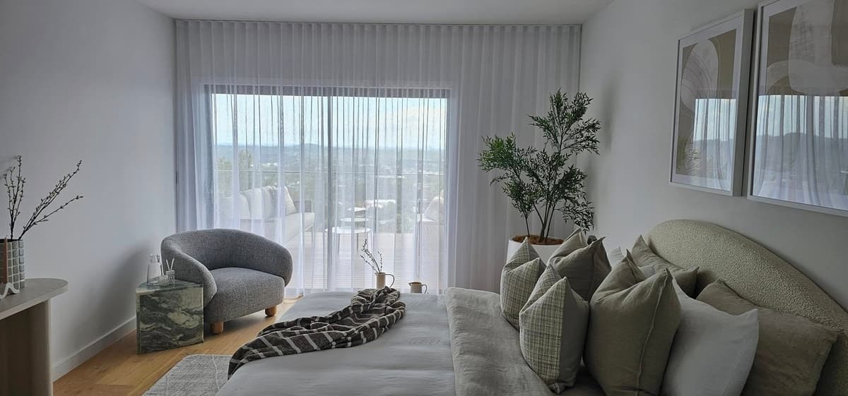 Wave fold sheer curtains hanging in even S-curves across a bedroom window overlooking the hinterland