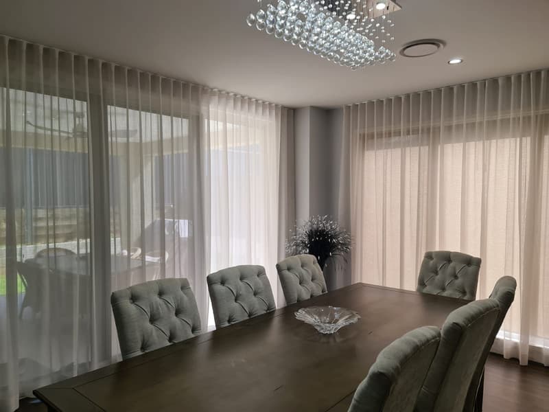 Wave-fold sheer curtains wrapping a dining room in soft afternoon light