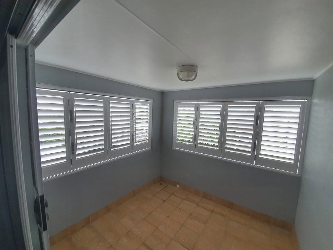 After: white plantation shutters fitted to the corner windows of a sunroom