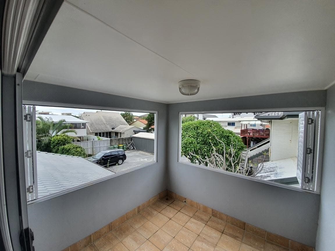 Before: the same sunroom with bare corner windows and no shutters