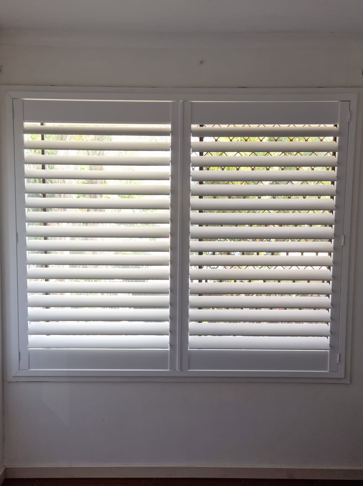 White PVC plantation shutters with louvres angled open across a window