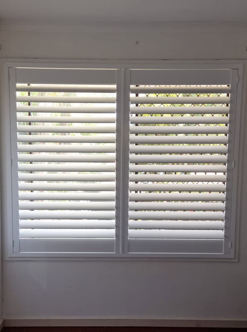 White plantation shutters with louvres angled open across a bedroom window